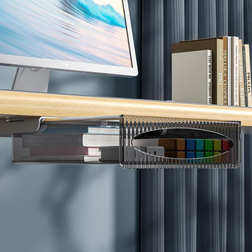 A modern desk with a monitor, books on the right, and a boîte de rangement à tiroir auto-adhésive sous table for extra office storage. Blue curtains in the background complete the calming look.